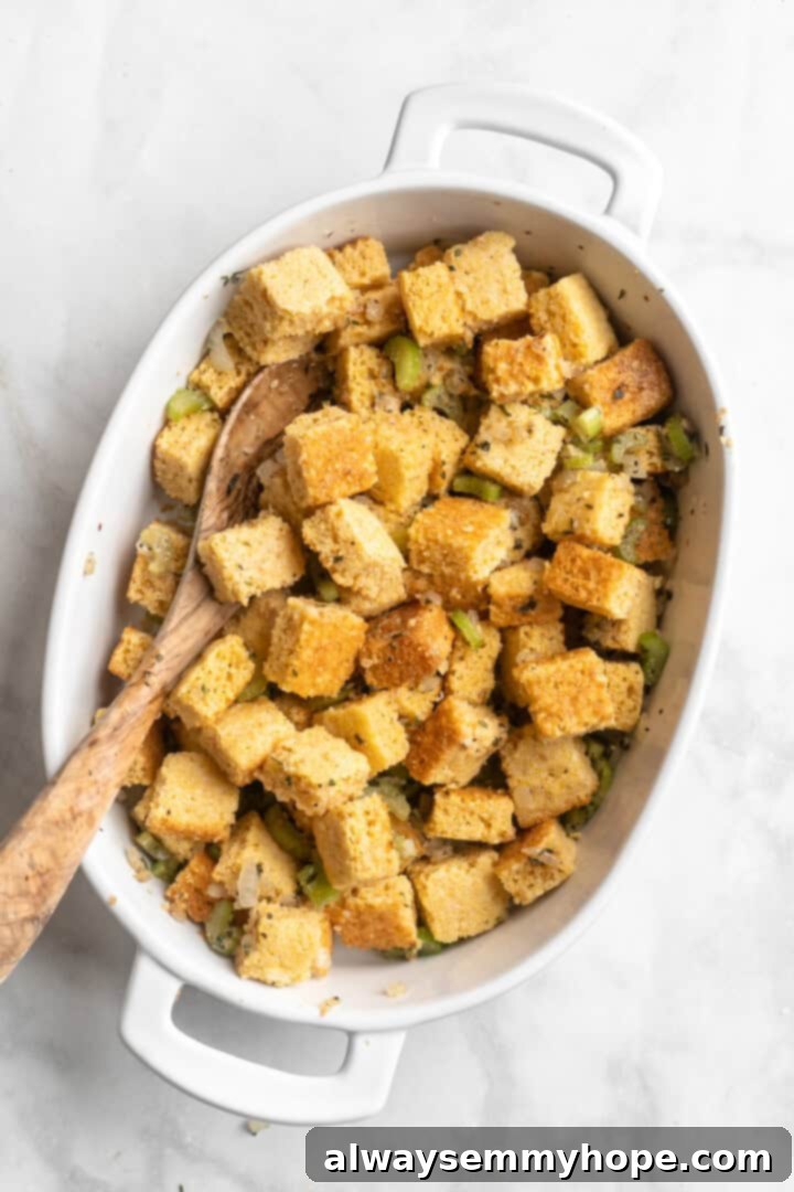 A person stirring together cornbread pieces, sautéed vegetables, and a flax egg in a large casserole dish, preparing the stuffing mixture