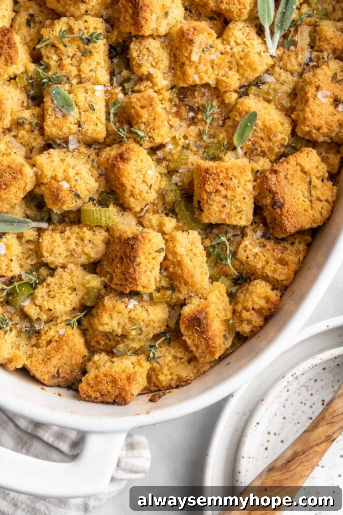Close-up overhead view of the golden-brown, crispy top of vegan cornbread stuffing in a large baking dish, garnished with fresh herbs