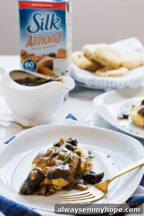 Creamy vegan mushroom gravy drizzled over mashed potatoes on a white plate with a fork on the side.
