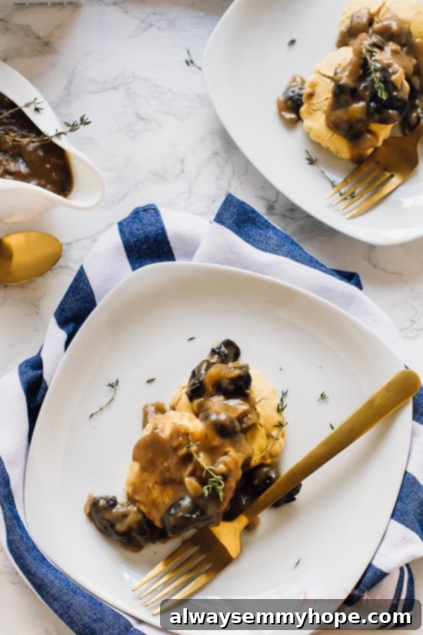 An inviting overhead shot of perfectly golden biscuits generously smothered in rich vegan mushroom gravy, with a minimalist gold fork waiting on the side.