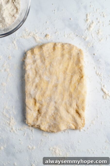 A rolled-out slab of vegan biscuit dough on a lightly floured white countertop, ready for folding.