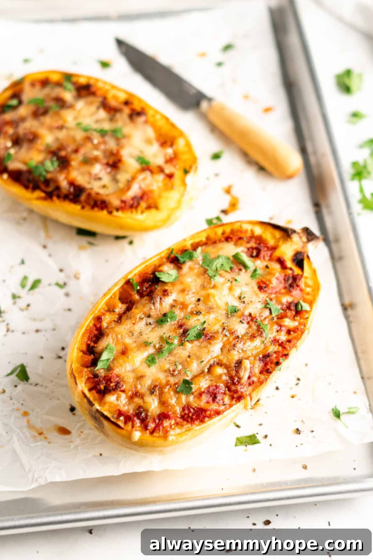 Two lasagna-stuffed spaghetti squash halves on parchment-lined baking sheet