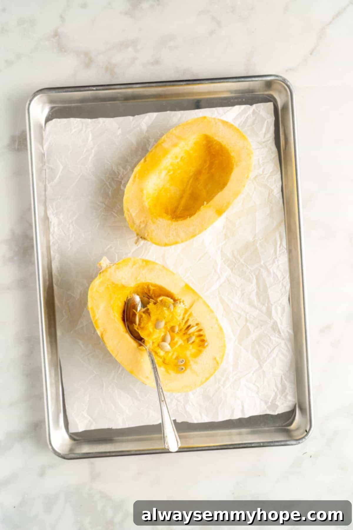 Overhead view of two spaghetti squash halves with spoon scooping out seeds