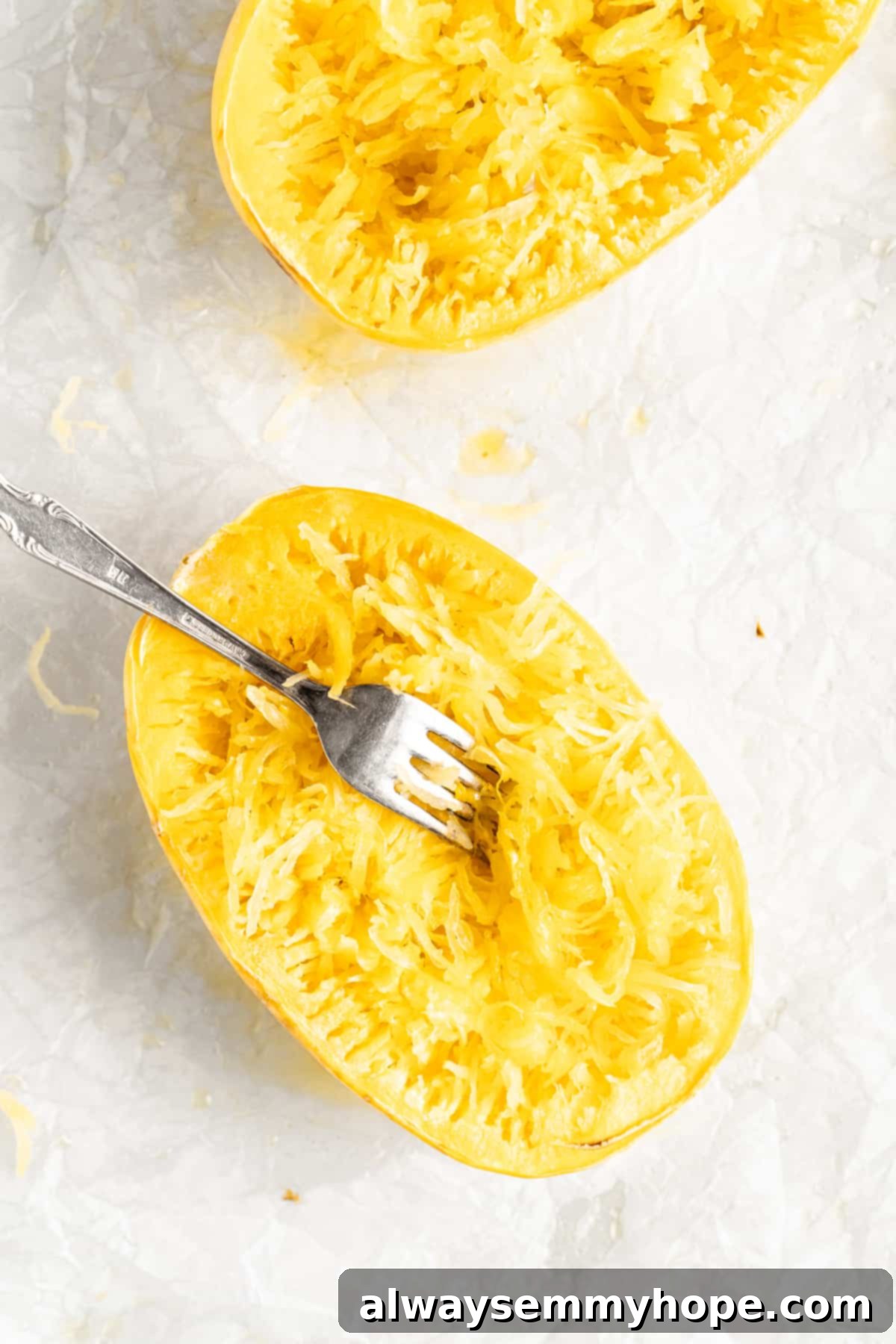 Two baked spaghetti squash halves with fork shredding flesh into noodles