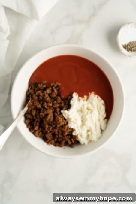 Vegan ricotta, crumbled meatloaf, and tomato sauce in bowl before being mixed
