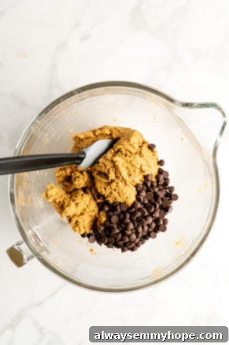 These vegan gluten-free chocolate chip cookies are an easy one-bowl recipe! Make soft, chewy, bakery-style cookies loaded with chocolate. Glass mixing bowl with cookie dough and chocolate chips