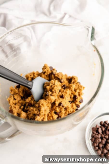 These vegan gluten-free chocolate chip cookies are an easy one-bowl recipe! Make soft, chewy, bakery-style cookies loaded with chocolate. Cookie dough being mixed in glass bowl with spatula