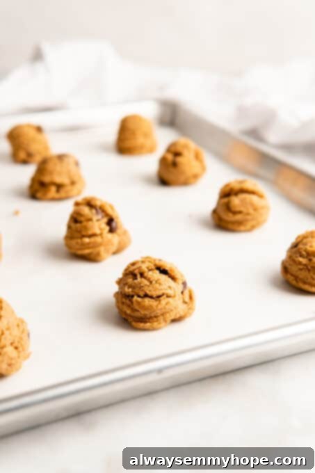 These vegan gluten-free chocolate chip cookies are an easy one-bowl recipe! Make soft, chewy, bakery-style cookies loaded with chocolate. Cookie dough balls on parchment-lined baking sheet