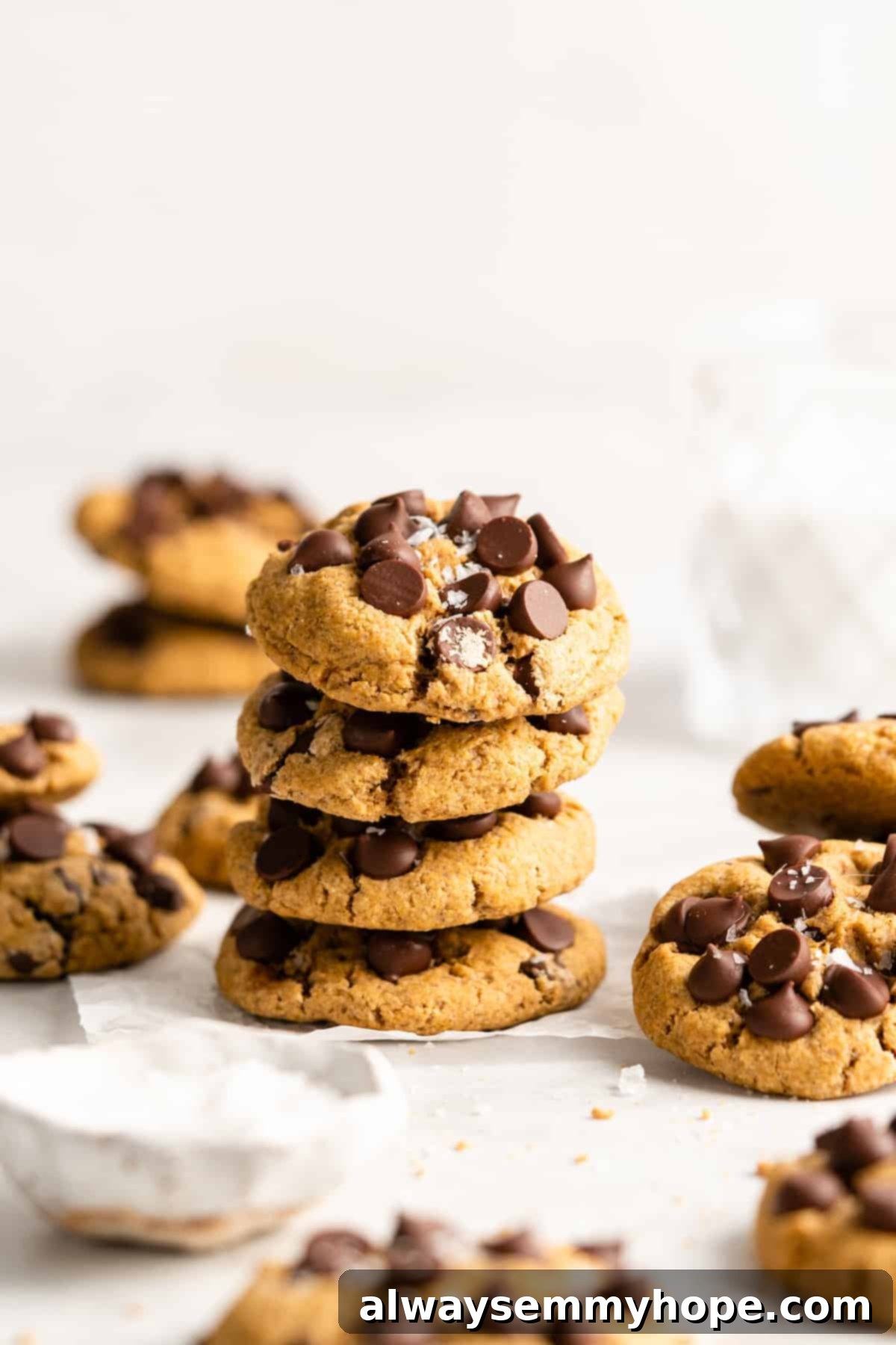 These vegan gluten-free chocolate chip cookies are an easy one-bowl recipe! Make soft, chewy, bakery-style cookies loaded with chocolate. Vegan gluten-free chocolate chip cookies stacked on a countertop next to more cookies.