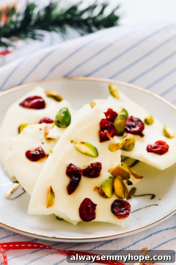 Chunks of white chocolate bark with cranberries and pistachio on a white plate. 