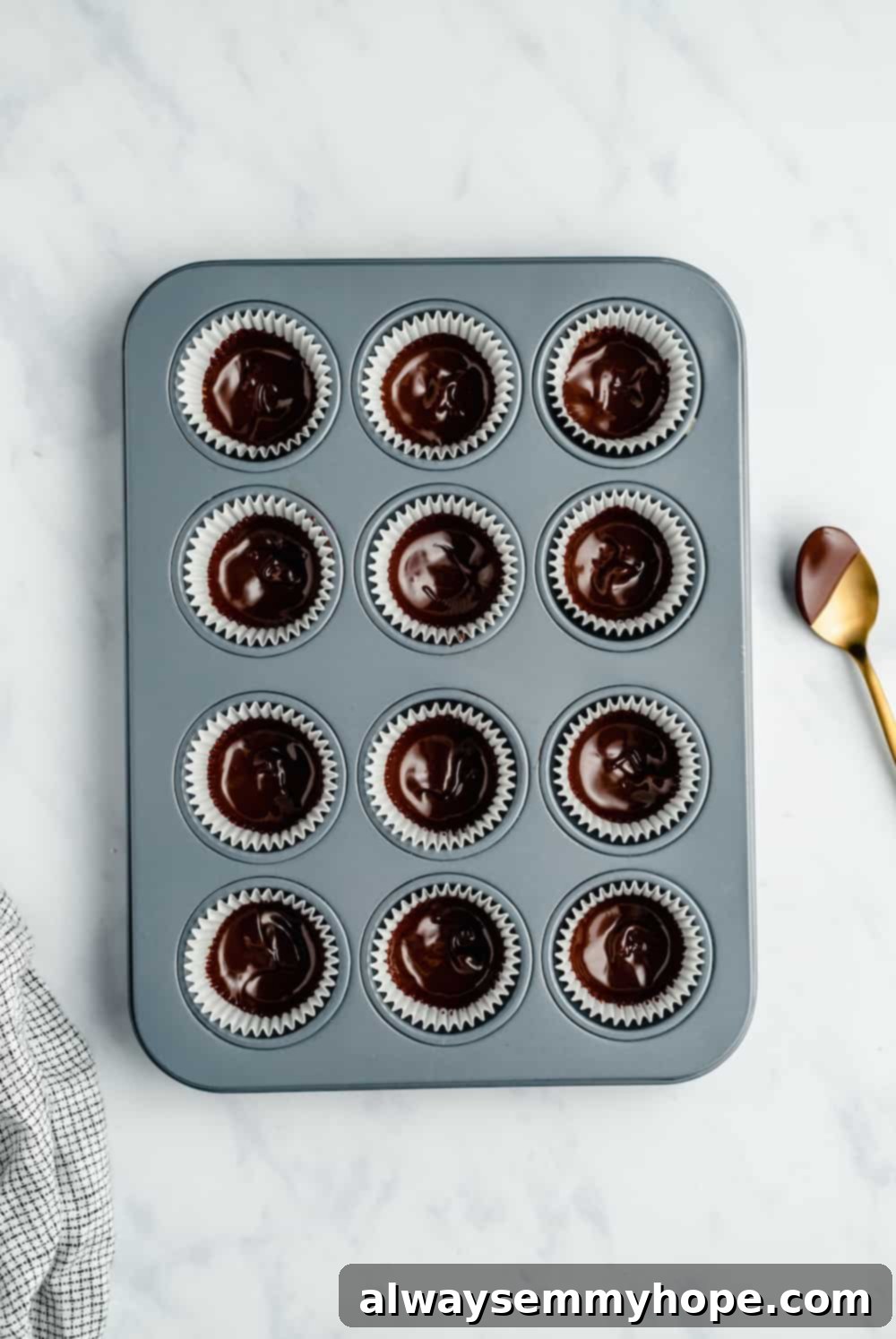 The first thin layer of melted chocolate spread evenly into mini muffin liners in a baking pan, ready for chilling.