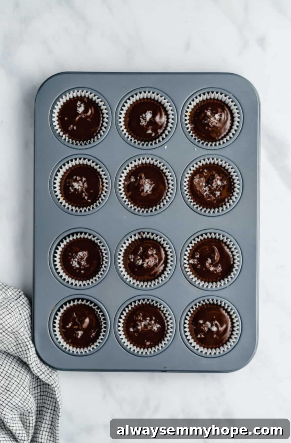 A mini muffin tin filled with fully assembled vegan peanut butter cups, topped with chocolate, ready to be chilled for final setting.