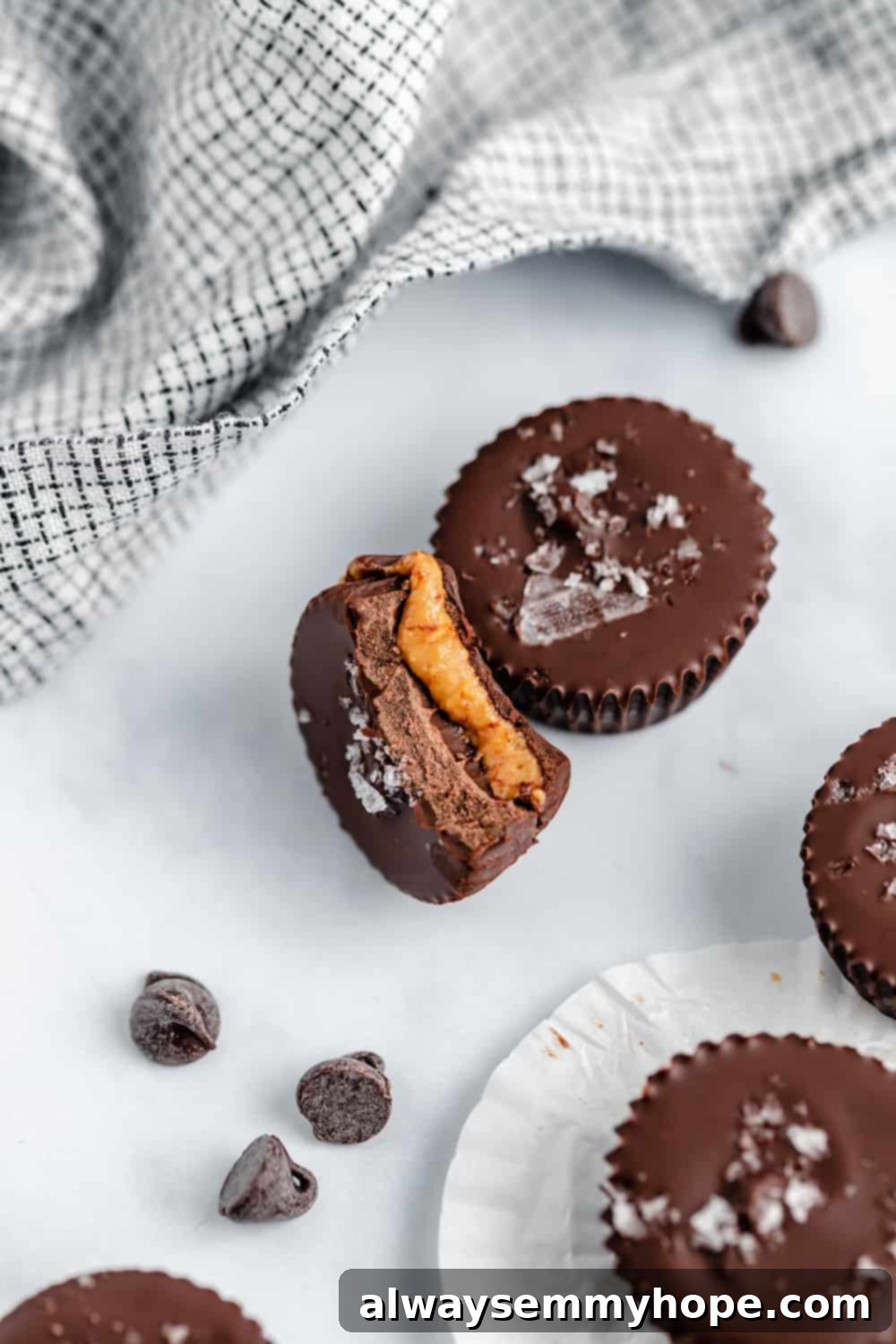 A whole vegan peanut butter cup next to one bitten in half, revealing the creamy peanut butter filling inside a dark chocolate shell.