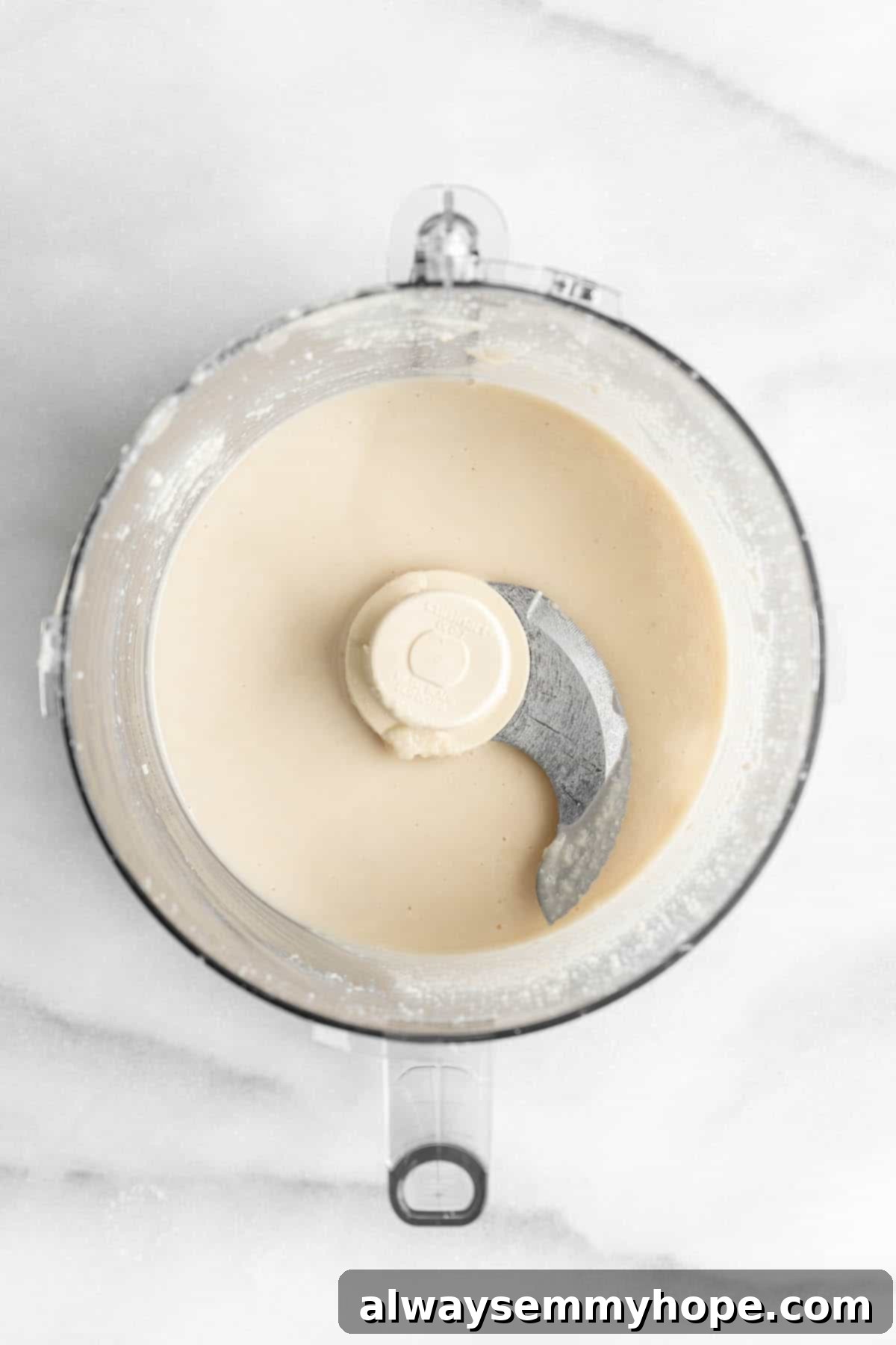 You won't believe how easy it is to make homemade coconut butter! All you need is a food processor, coconut flakes, and this simple tutorial. Coconut butter in a food processor bowl.