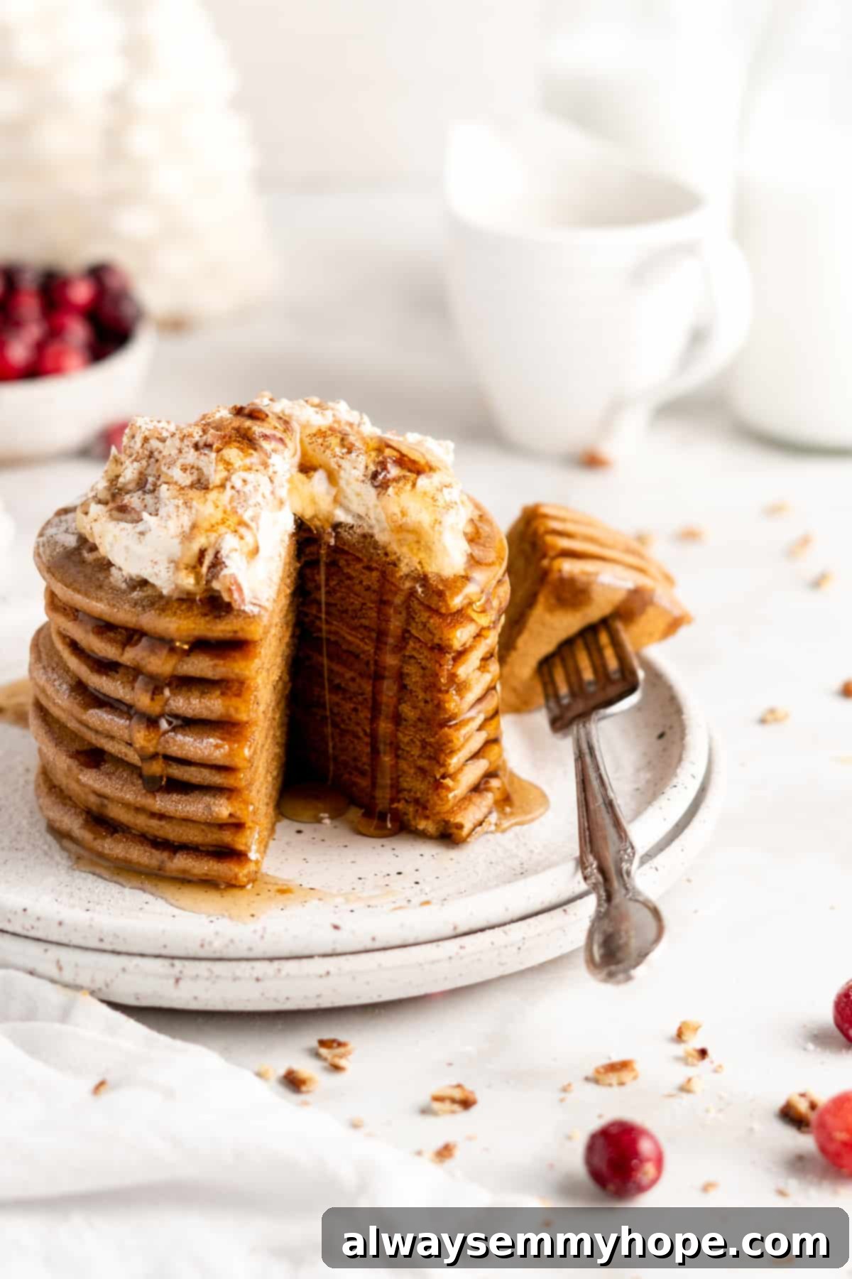 A stack of golden-brown vegan gingerbread pancakes, elegantly topped with a generous swirl of coconut whipped cream and a delicate drizzle of maple syrup, against a warm background.