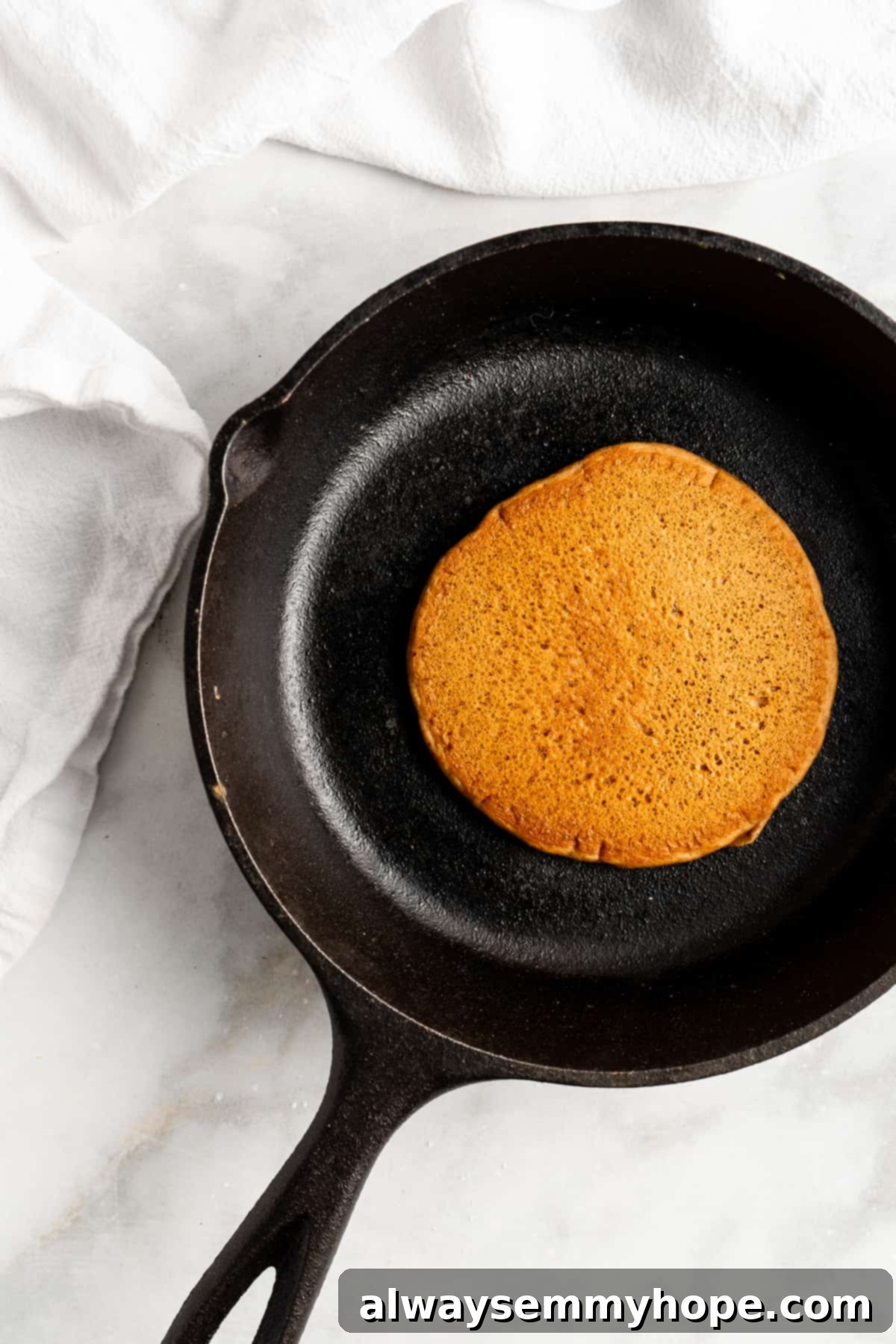 A perfectly formed vegan gingerbread pancake sizzling in a hot cast iron skillet, golden brown and ready to flip.