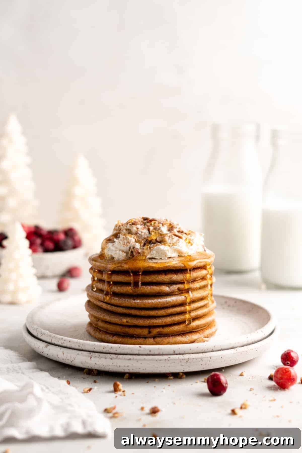 A delectable stack of vegan gingerbread pancakes, generously topped with maple syrup, fluffy coconut whipped cream, and chopped nuts, ready to be enjoyed.