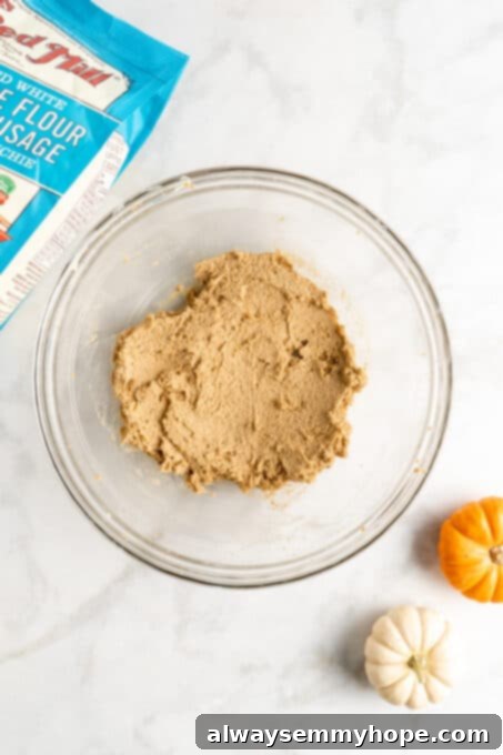 These easy vegan pumpkin cookies are ultra-soft. Made with 10 ingredients, they're topped with an irresistible cream cheese frosting, too! The cookie dough in a bowl after vanilla extract and pumpkin puree are thoroughly mixed, showing its smooth, uniform texture.