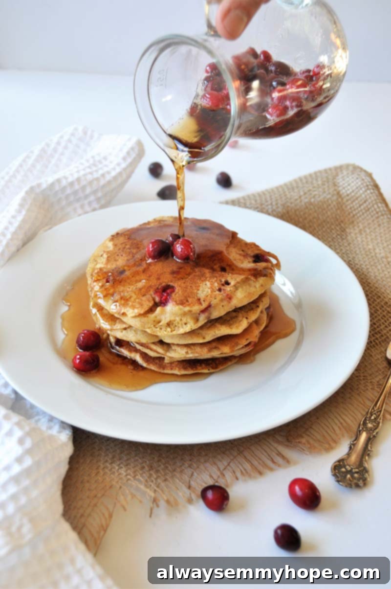 Vegan Christmas Delights: 50 Festive Plant-Based Meals 5 Pouring syrup on a stack of orange cranberry pancakes.