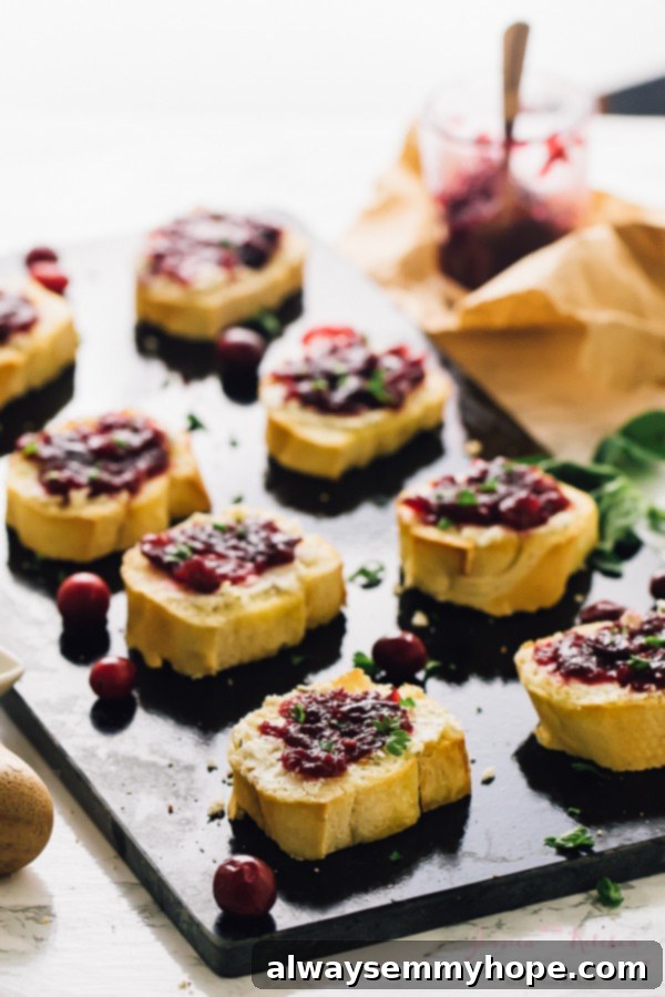 Cranberry goat cheese crostini on a black slate, adorned with fresh cranberries for a festive touch.
