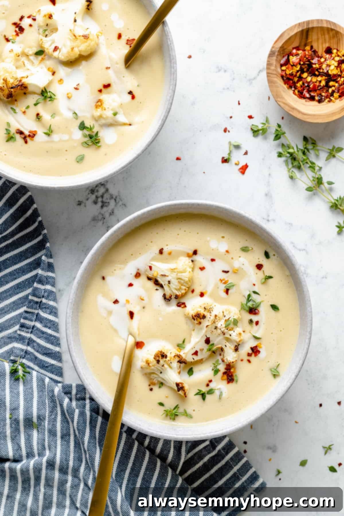 Velvety Roasted Cauliflower Soup 11 Overhead view of two bowls filled with cauliflower soup, garnished with red pepper flakes, thyme, and coconut milk