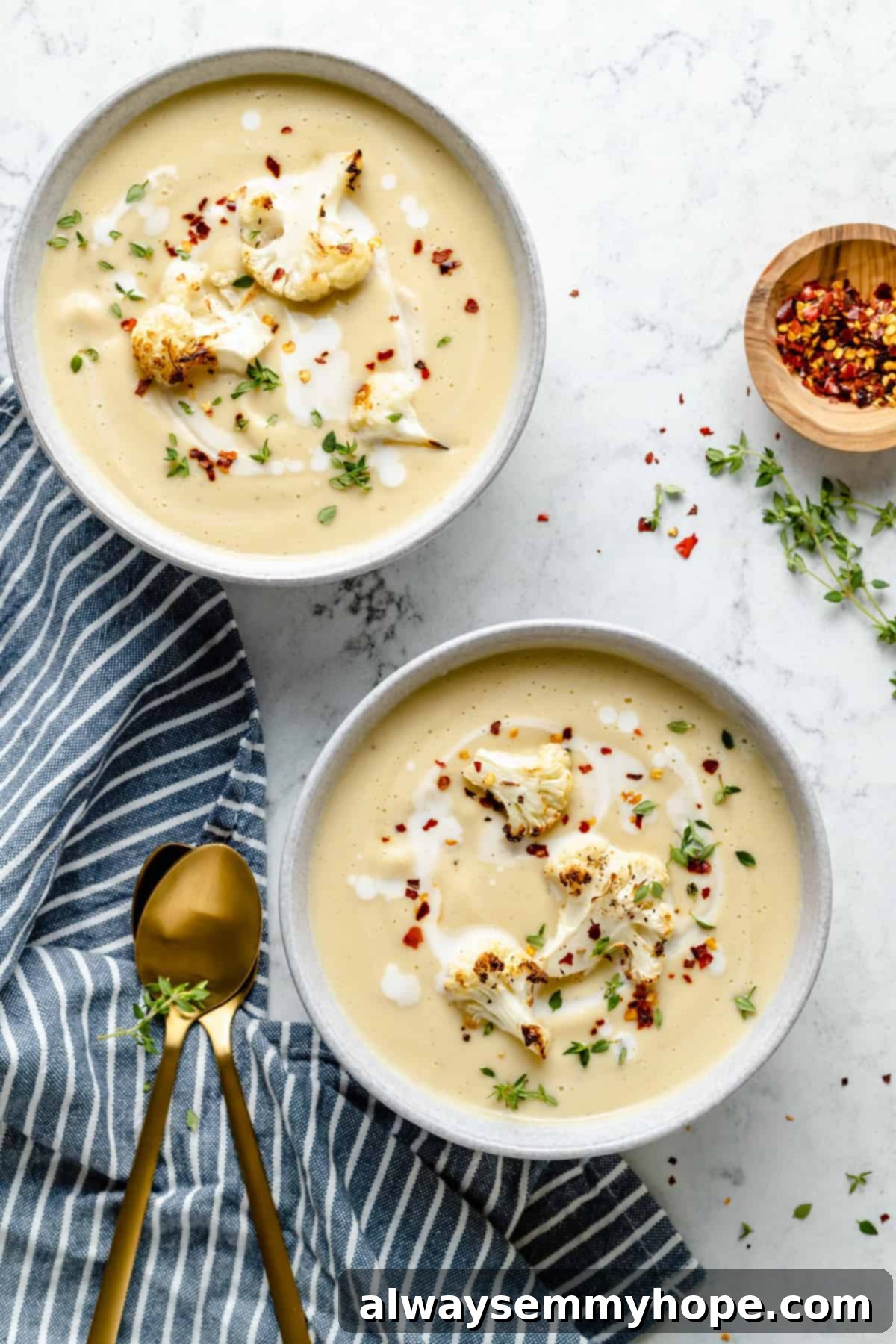 Velvety Roasted Cauliflower Soup 13 Overhead view of two bowls of Roasted Cauliflower Soup with striped cloth napkin and gold spoons