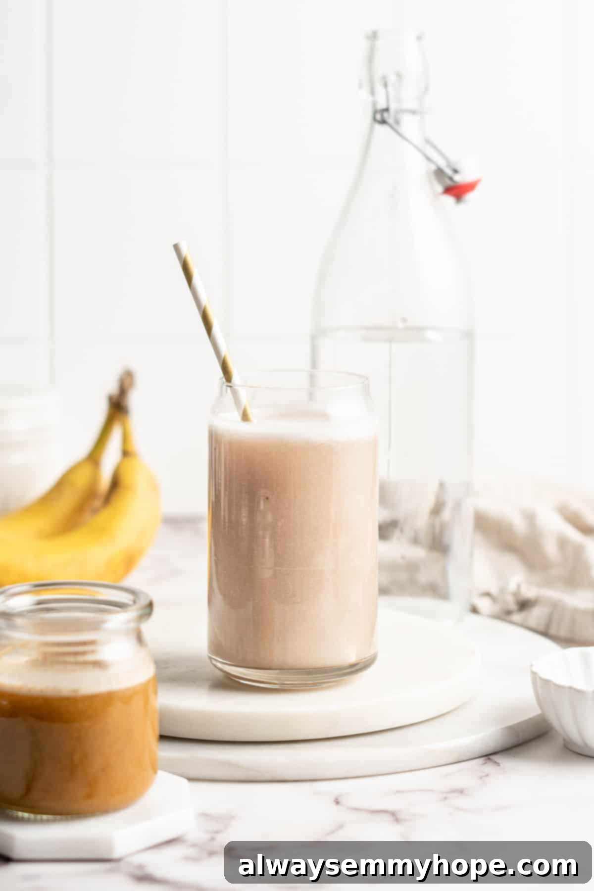 Freshly made banana milk in a glass jar with a straw, placed on a wooden surface.