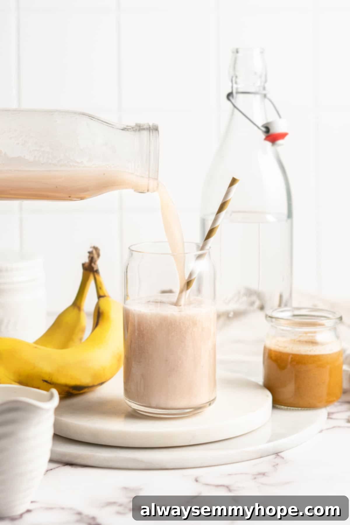 Freshly blended banana milk being poured from a blender into a glass jar with a straw.