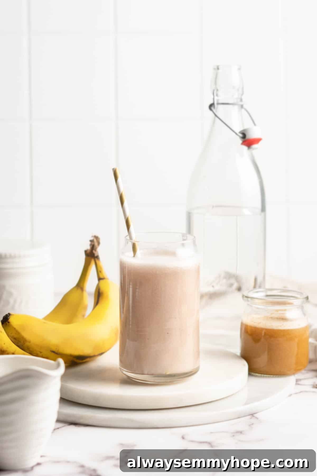 Freshly made banana milk in a clear glass jar with a straw, placed on a light wooden surface.