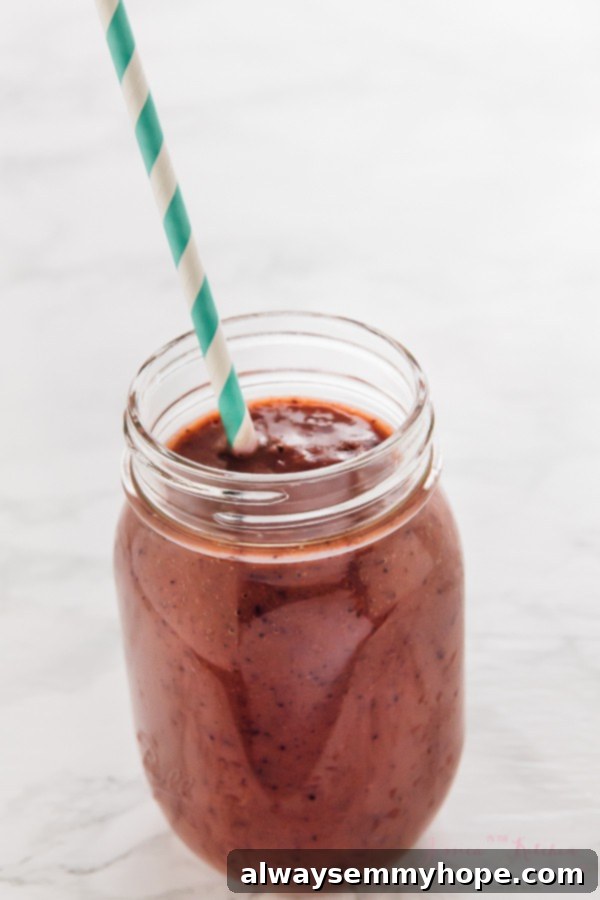 7 Simple and Speedy Vegan Banana Smoothies 12 A delightful mixed berry smoothie in a glass mason jar with a straw, brimming with antioxidants and flavor.