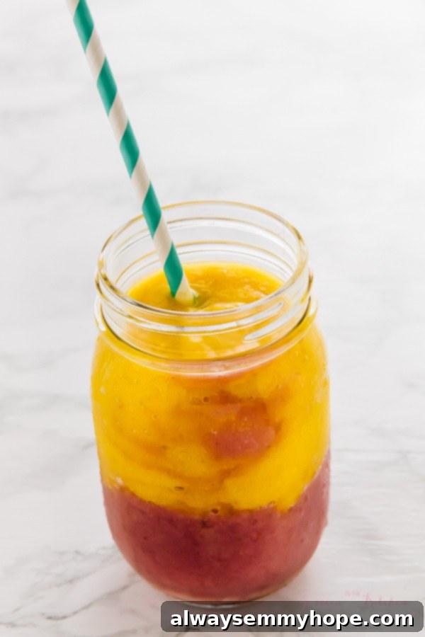7 Simple and Speedy Vegan Banana Smoothies 13 A beautiful layered strawberry mango smoothie in a glass mason jar with a straw, featuring distinct fruit layers.