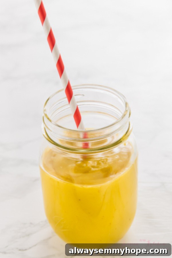 7 Simple and Speedy Vegan Banana Smoothies 15 A bright yellow turmeric mango smoothie in a glass jar with a red straw, highlighting its vibrant color and healthy ingredients.
