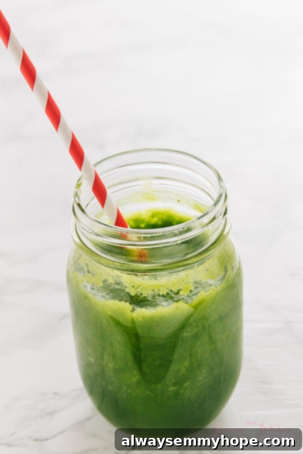 7 Simple and Speedy Vegan Banana Smoothies 8 A vibrant tropical green smoothie served in a mason jar with a straw, placed on a white surface.
