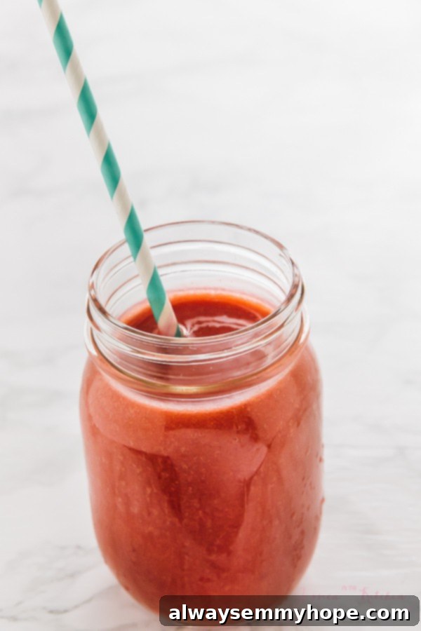 7 Simple and Speedy Vegan Banana Smoothies 10 A vibrant red strawberry banana smoothie in a mason jar with a striped straw, ready to be enjoyed.