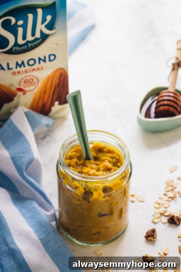 Pumpkin overnight oats in a jar with a spoon and a carton of almond milk in the background. 