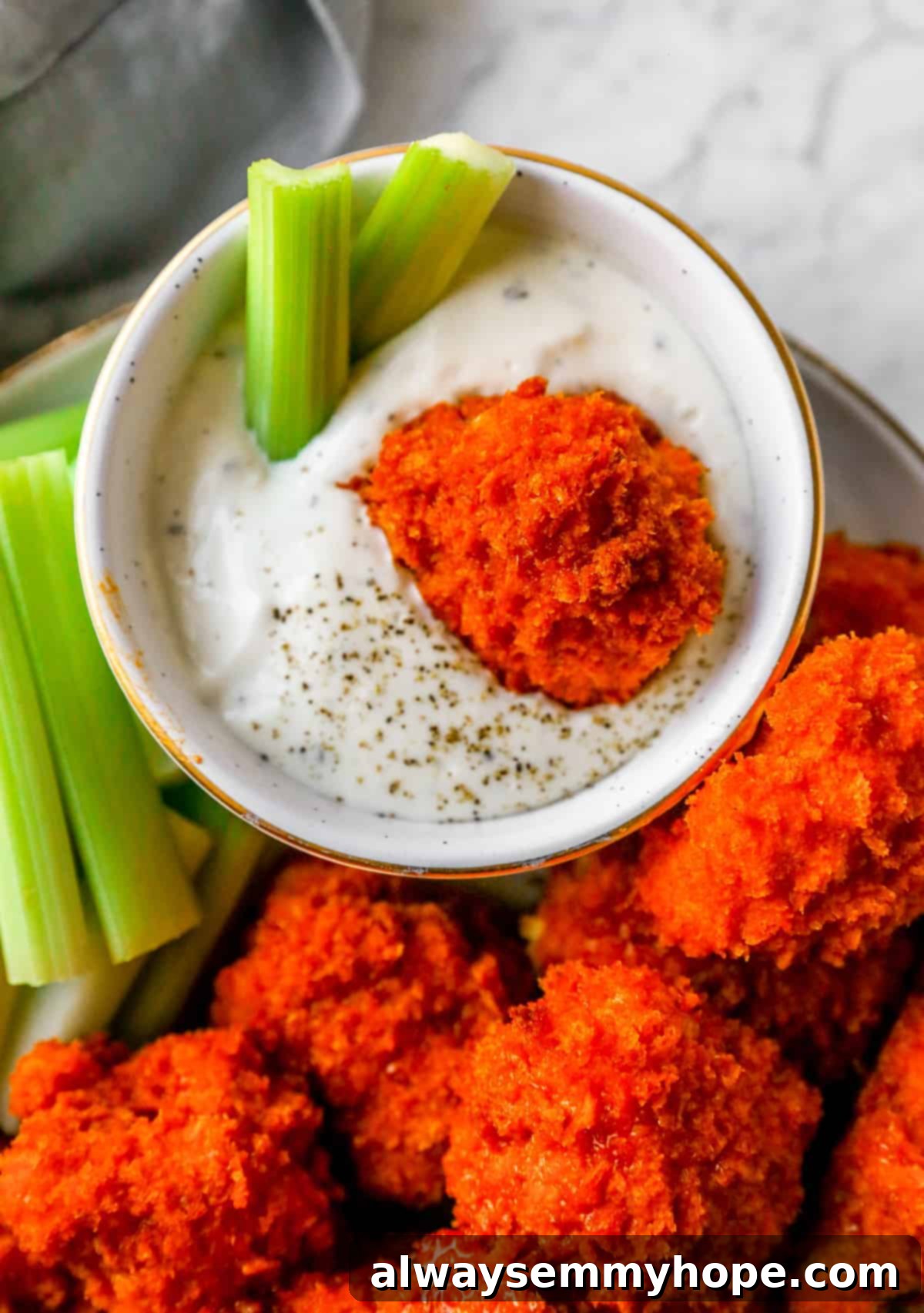 Buffalo cauliflower wings are the best vegan appetizer for game day! They're spicy and oven-baked to crispy perfection. Yum! A crispy buffalo cauliflower wing being dipped into a creamy ranch dressing, with fresh celery stalks on the side.