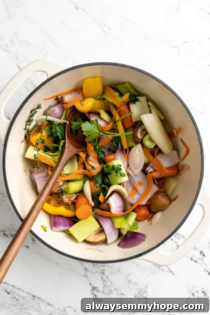 Learn how to make vegetable broth with veggie scraps. It’s the best broth you'll ever have, plus easy, cost-effective, and freezer-friendly! Overhead view of ingredients for vegetable broth in pot with wooden spoon