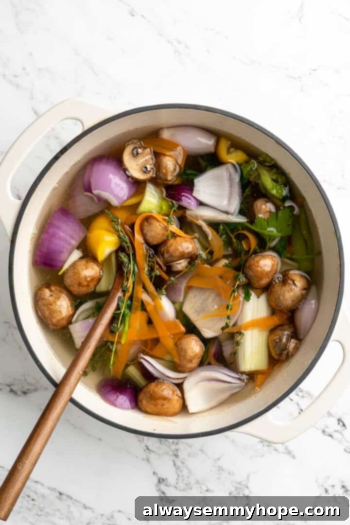 Learn how to make vegetable broth with veggie scraps. It’s the best broth you'll ever have, plus easy, cost-effective, and freezer-friendly! Overhead view of vegetable broth in pot with wooden spoon