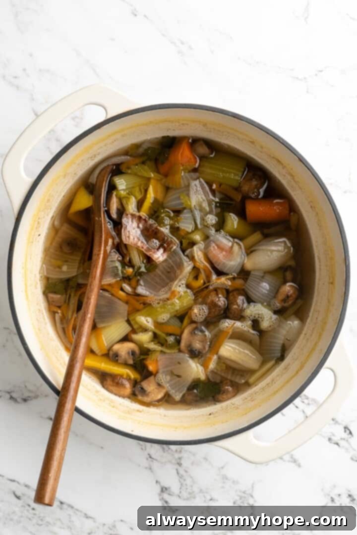 Learn how to make vegetable broth with veggie scraps. It’s the best broth you'll ever have, plus easy, cost-effective, and freezer-friendly! Overhead view of finished vegetable broth in pot with wooden spoon