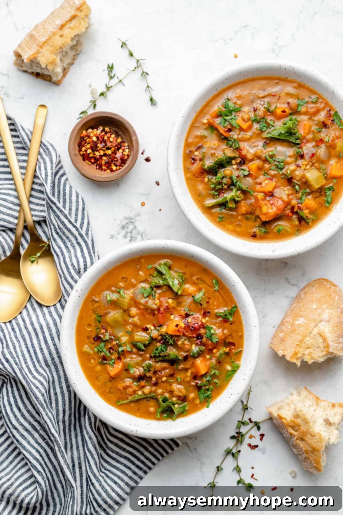 Overhead view of two bowls of lentil soup on marble board with baguette pieces and garnishes