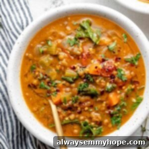 Overhead view of chunky lentil soup in white bowl with gold spoon
