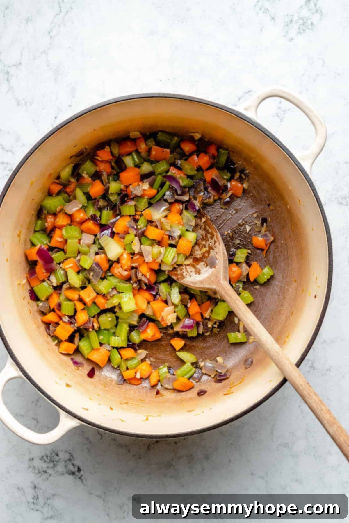 Overhead view of celery, carrots, and onions in large pot with wooden spoon