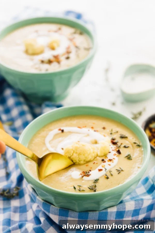 A spoon dipping into a bowl roasted cauliflower soup.