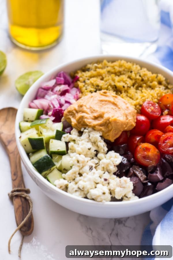 A mediterranean quinoa bowl on a table with lime wedges.