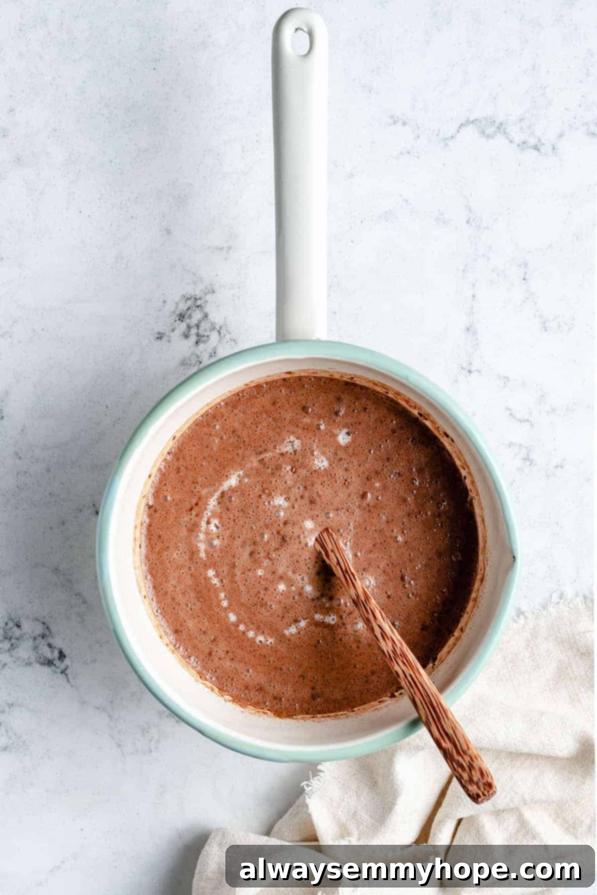 Overhead view of vegan hot chocolate gently simmering in a saucepan, looking rich and ready.