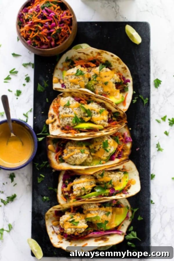 Overhead shot of cauliflower tacos on a black slat with sauce and slaw on the side. 