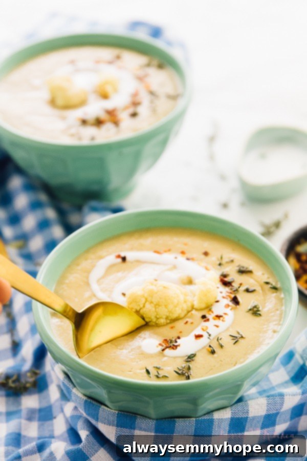 Two bowls of roasted cauliflower soup with a golden spoon dipping in.