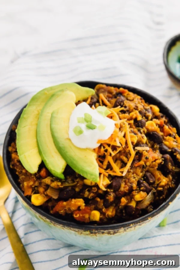 Vegan chili in a blue bowl with sour cream and slices of avocado on top. 