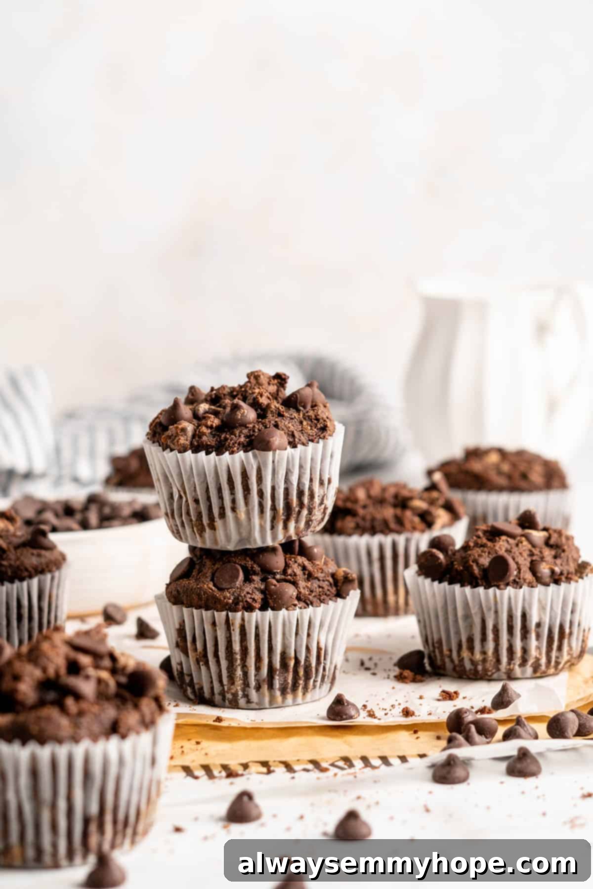 These easy chocolate banana muffins are moist, soft, and bursting with chocolate. They're made without refined sugar, gluten-free, and vegan! Two stacked chocolate banana muffins surrounded by more muffins on a countertop.