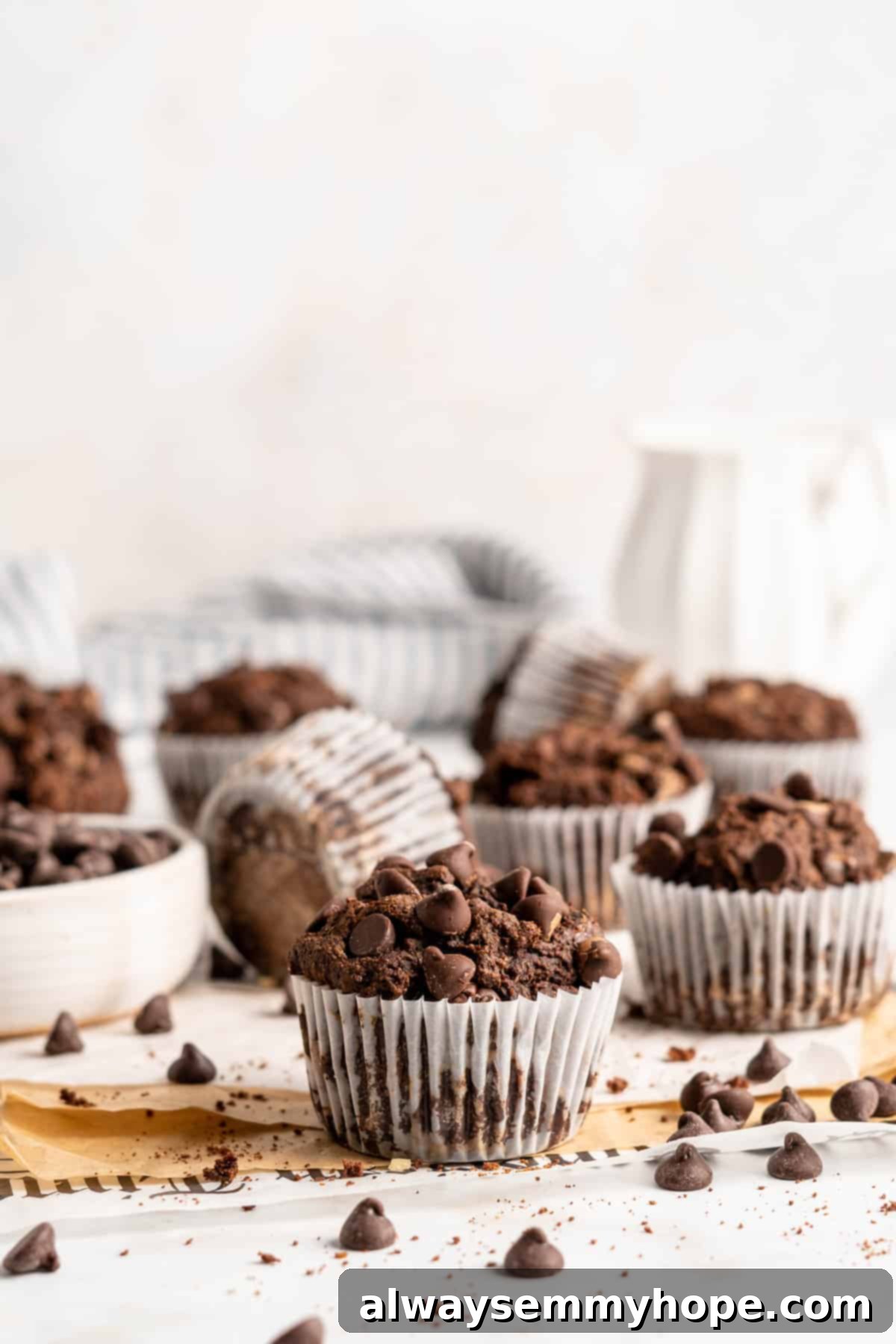 These easy chocolate banana muffins are moist, soft, and bursting with chocolate. They're made without refined sugar, gluten-free, and vegan! Assorted double chocolate banana muffins in white muffin wrappers on a countertop, surrounded by scattered chocolate chips.